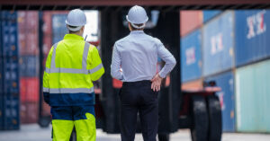 Two people standing in a shipping port looking at cargo containers